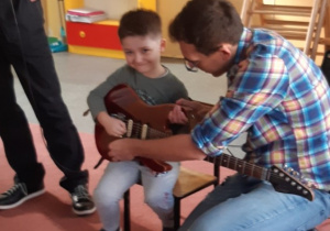 chłopiec trzyma gitarę a muzyk mu pomaga zagrać